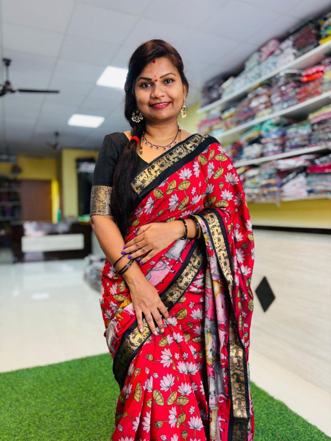 Woman in a red saree with floral patterns standing in a store.