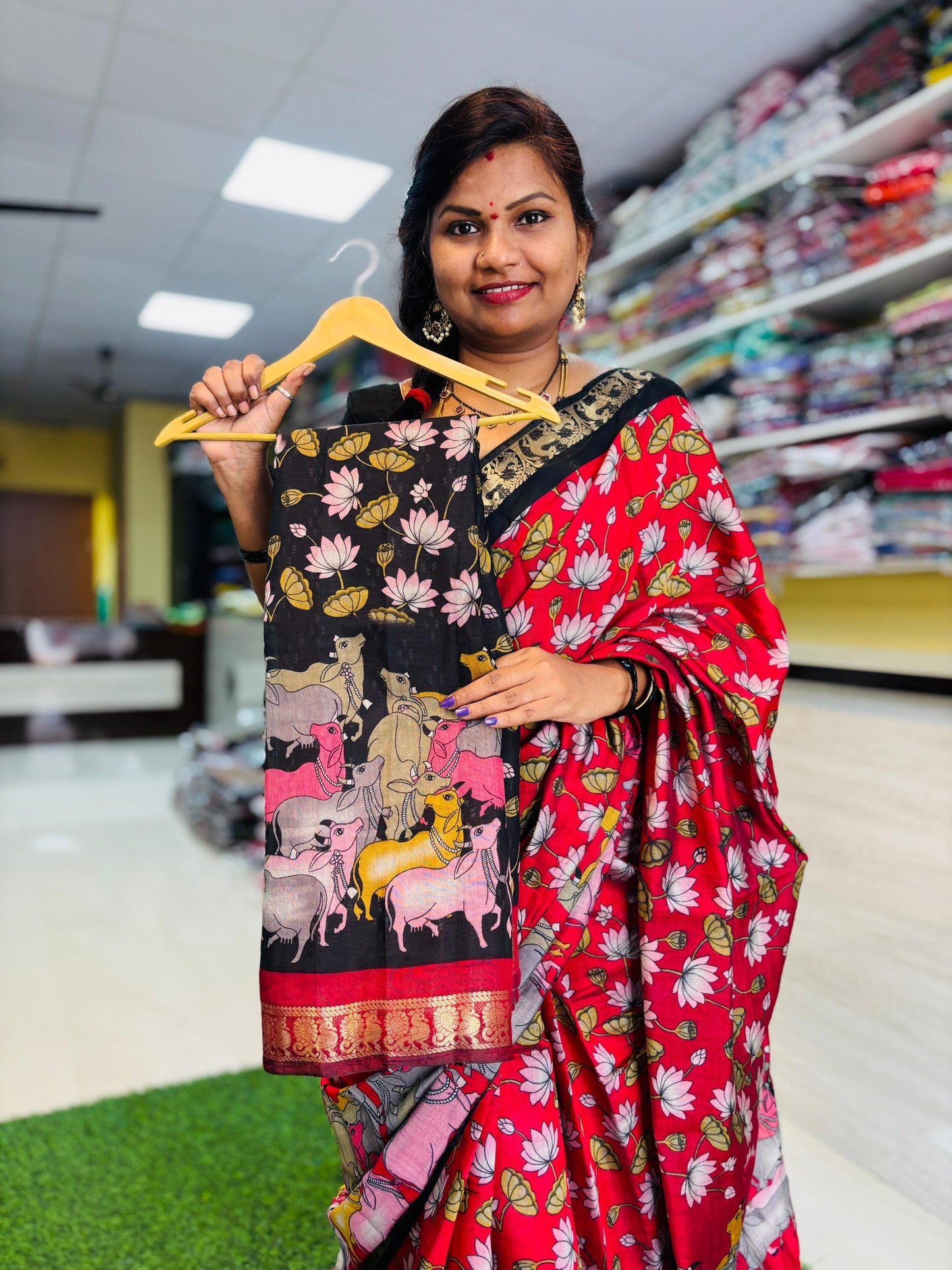 Woman holding a hanger with a black saree featuring animal designs in a store setting